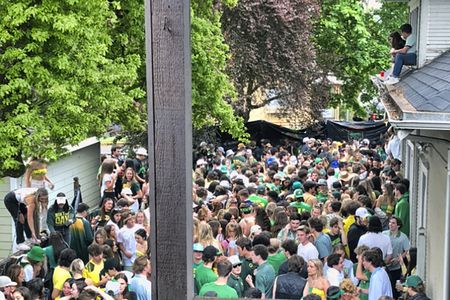 A large group of people clustered together  in a yard. Many are wearing green hats or shirts.